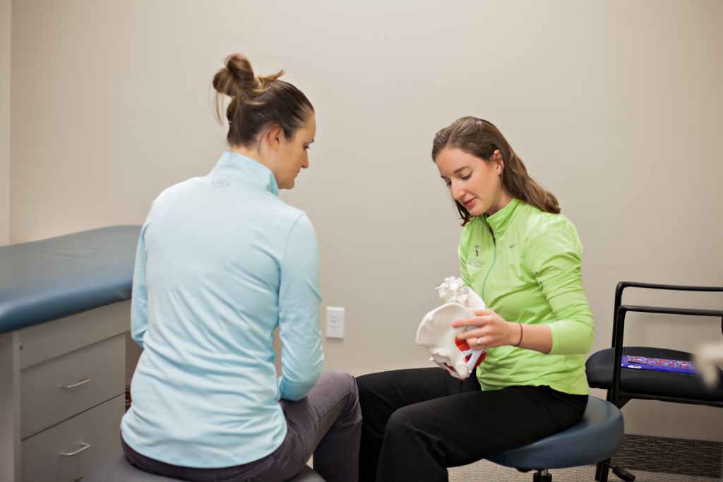 Chiropractor educates woman about the pelvis holding a skeleton hip