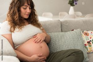 Pregnant woman holding her baby belly while sitting on a grey couch