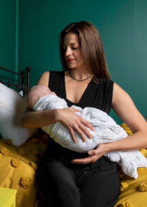 Michelle from Gold Coast Doulas holding a sleeping baby on a yellow bed with green walls in the background
