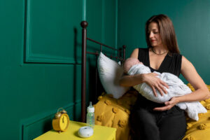 Michelle from Gold Coast Doulas holding a swaddled baby on a yellow bed with green walls
