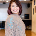 Regina Lum wearing mauve and teal clothing smiles in front of a studio