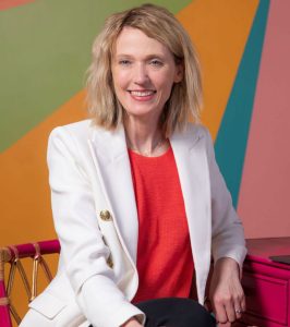 Kristin sitting in white jacket in front of colorful geometric background