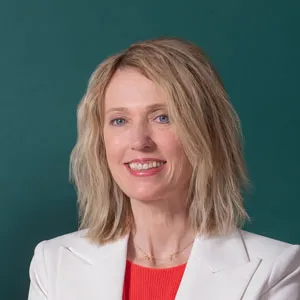 Kristin Revere smiling for a photo in a white jacket and red shirt in front of a green background