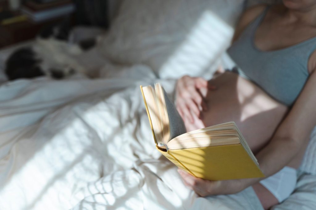 Pregnant woman laying in bed reading a book