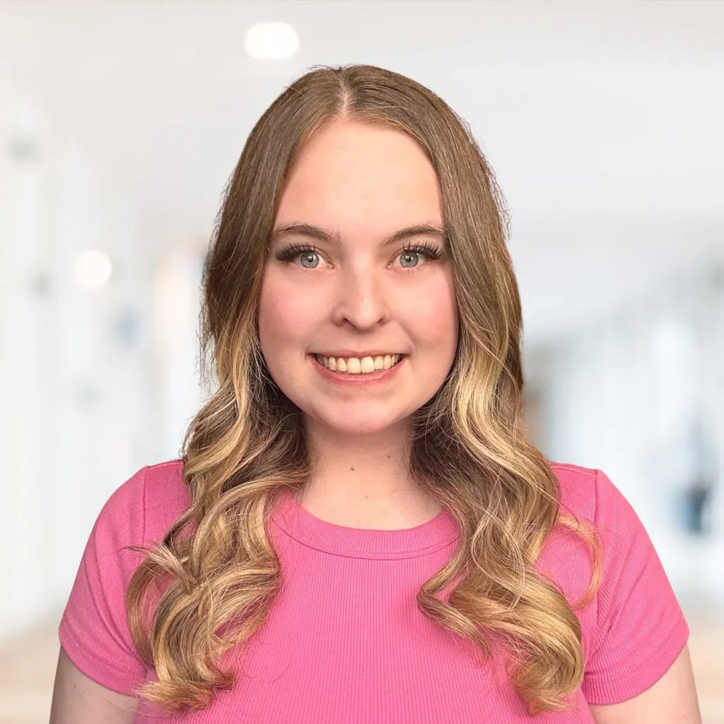 Brielle smiling headshot wearing a pink shirt in front of a white blurred background