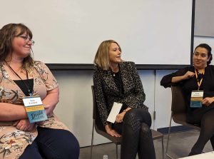 Three women sitting in chairs holding books at an event