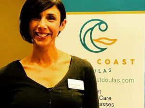 Alyssa smiling for a picture with a black shirt and a name tag in front of a Gold Coast Doulas banner