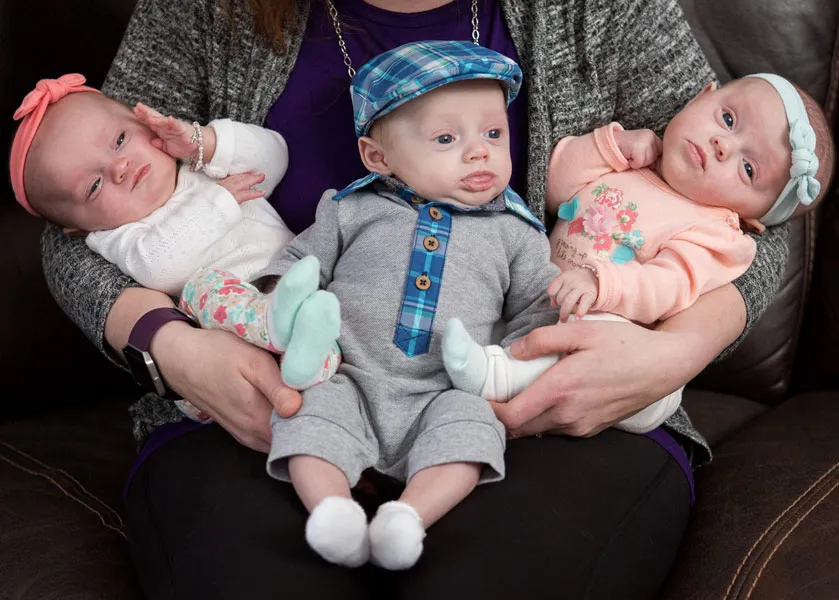 Triplet babies in outfits being held by a caregiver