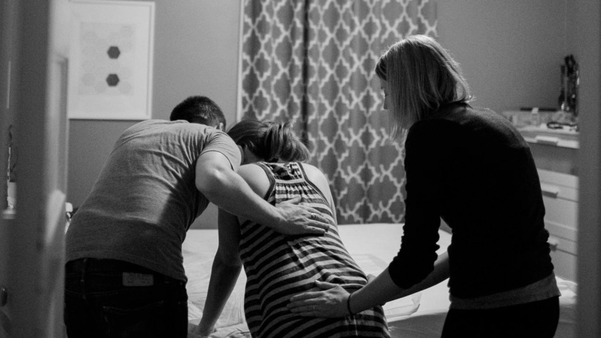 Woman in labor holding herself on a bed while her partner and a Doula support her back