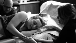 Woman in labor lying down on a bed holding the hand of a Doula