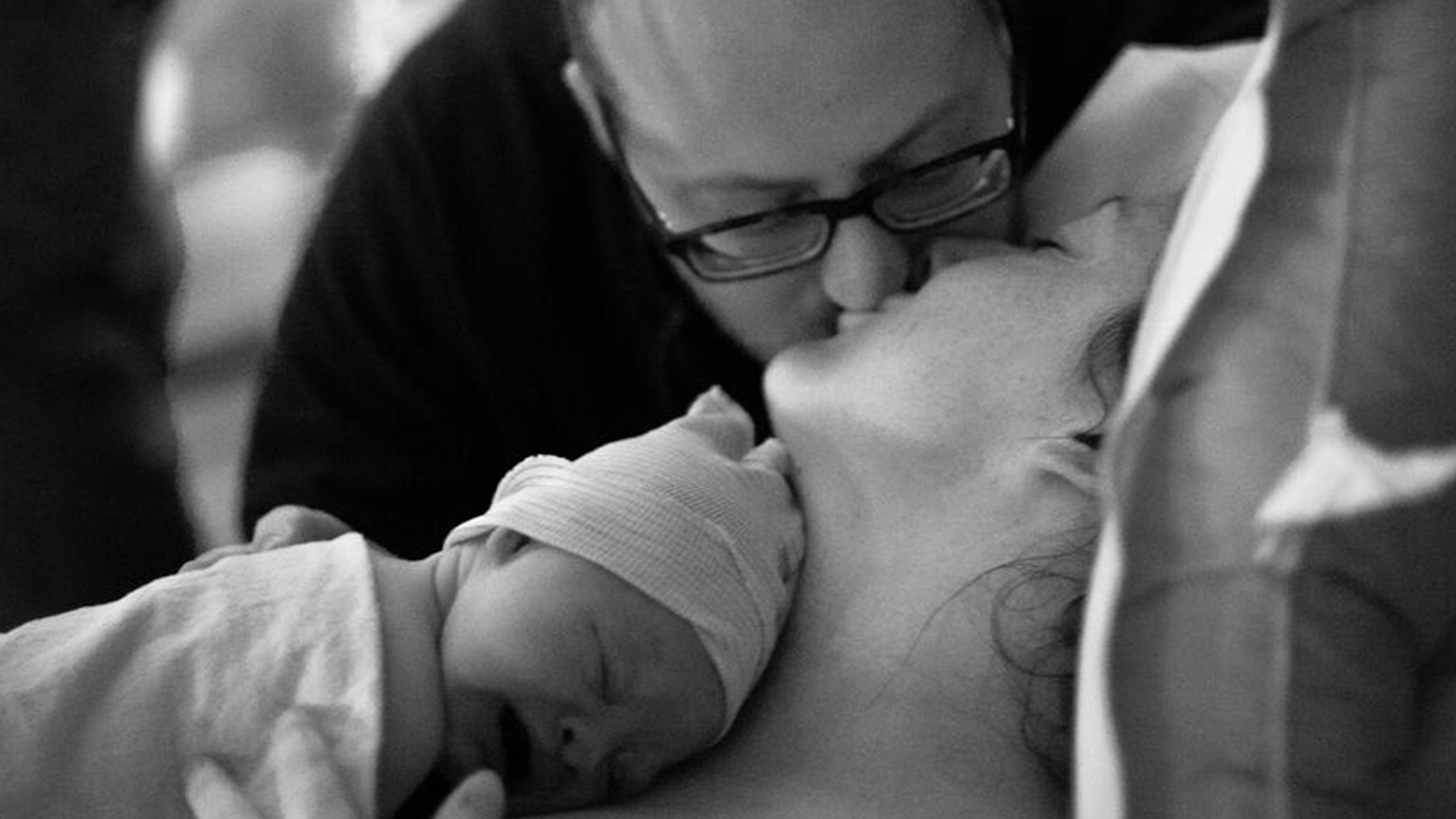 Man kissing his partner after she gave birth while holding a newborn